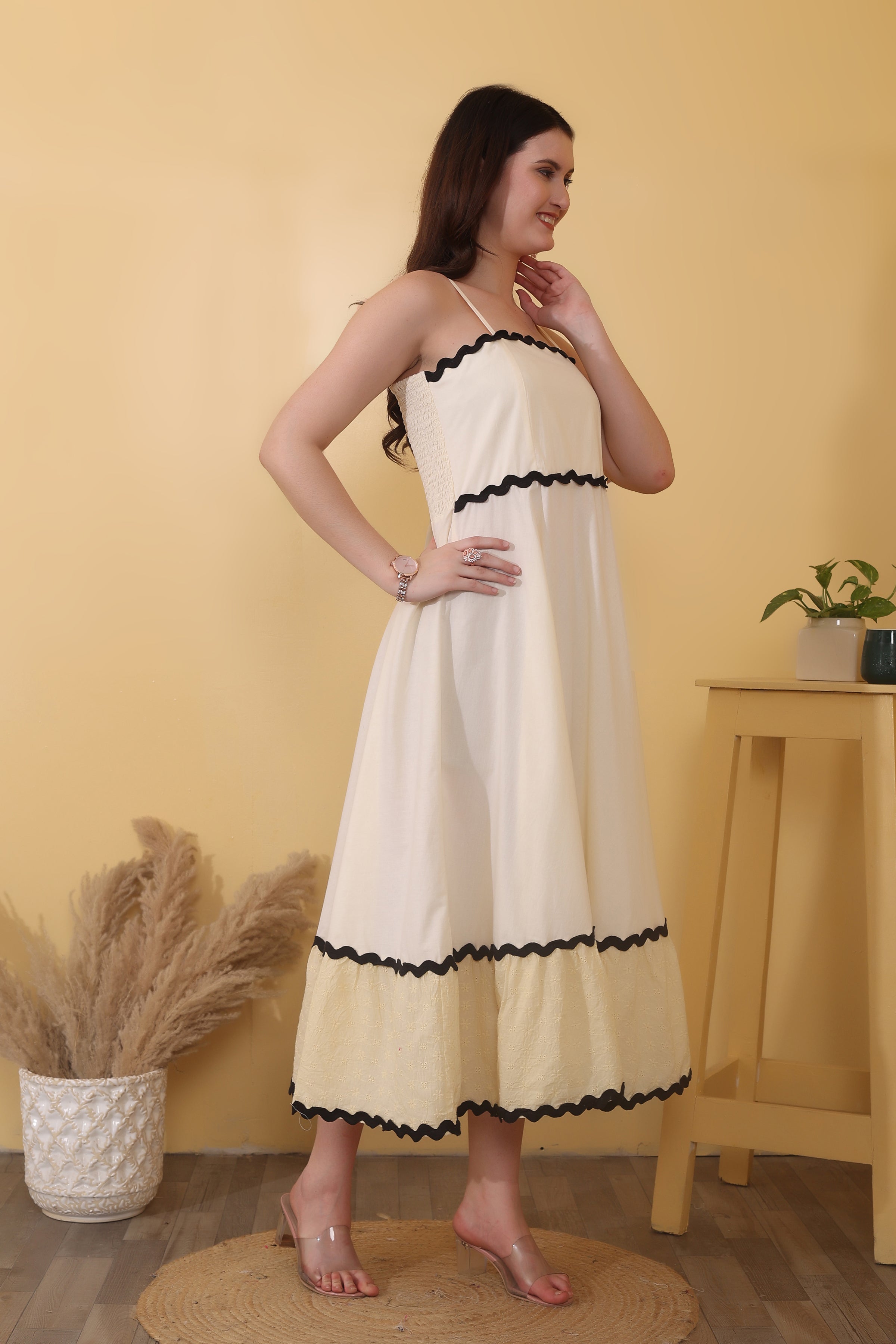Cream maxi dress crafted from 100% cotton poplin with Schiffli cotton tiers, featuring a straight neckline with adjustable spaghetti straps, smocked back, tiered hem, and bold black ric-rac trim.