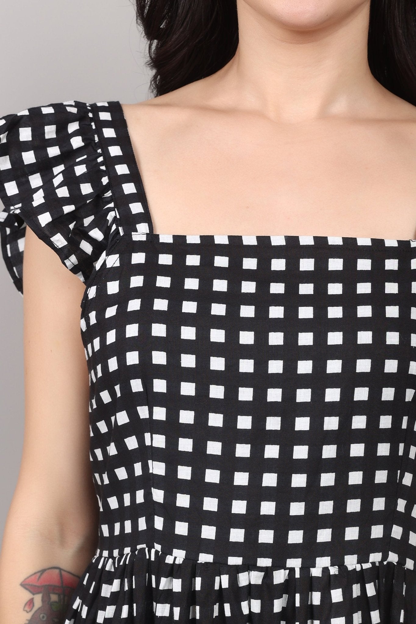 Black-and-white gingham cotton midi dress with square neckline, ruffled cap sleeves, fit-and-flare silhouette, tiered skirt, and a fixed bow at the back.