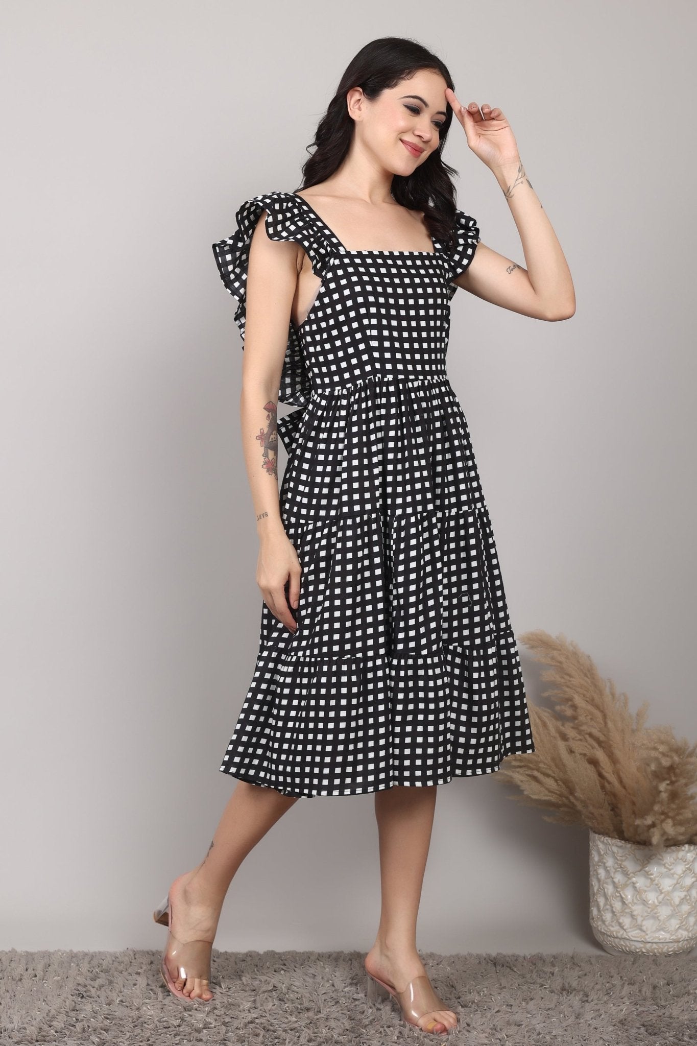 Black-and-white gingham cotton midi dress with square neckline, ruffled cap sleeves, fit-and-flare silhouette, tiered skirt, and a fixed bow at the back.
