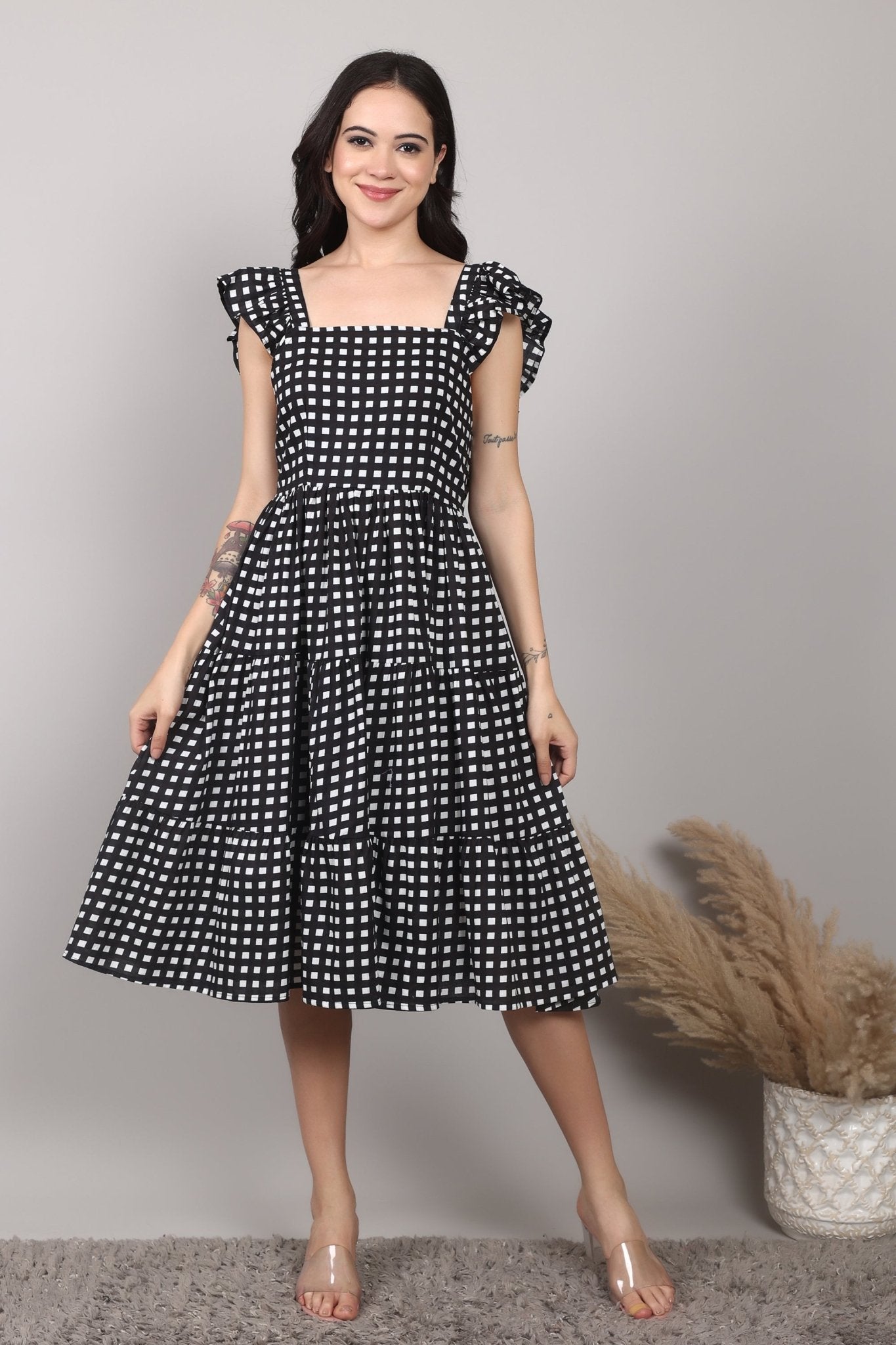 Black-and-white gingham cotton midi dress with square neckline, ruffled cap sleeves, fit-and-flare silhouette, tiered skirt, and a fixed bow at the back.