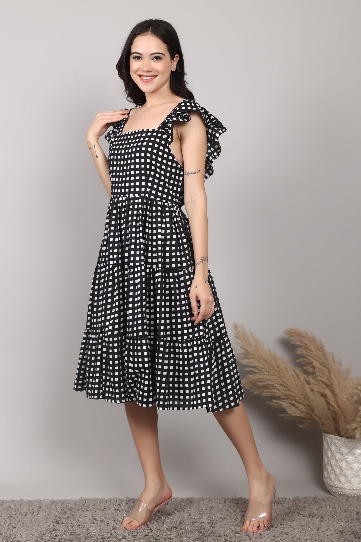 Black-and-white gingham cotton midi dress with square neckline, ruffled cap sleeves, fit-and-flare silhouette, tiered skirt, and a fixed bow at the back.