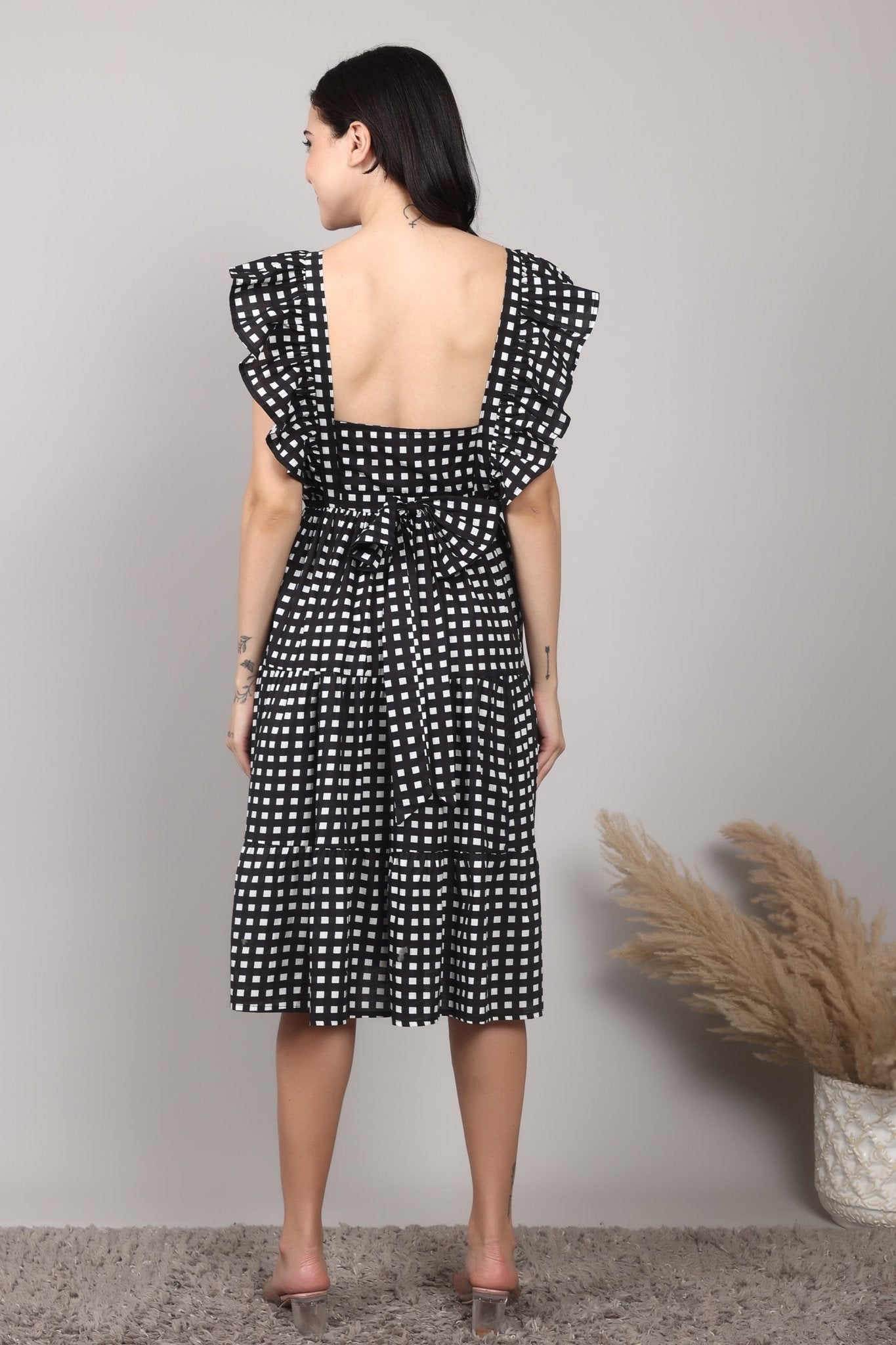 Black-and-white gingham cotton midi dress with square neckline, ruffled cap sleeves, fit-and-flare silhouette, tiered skirt, and a fixed bow at the back.