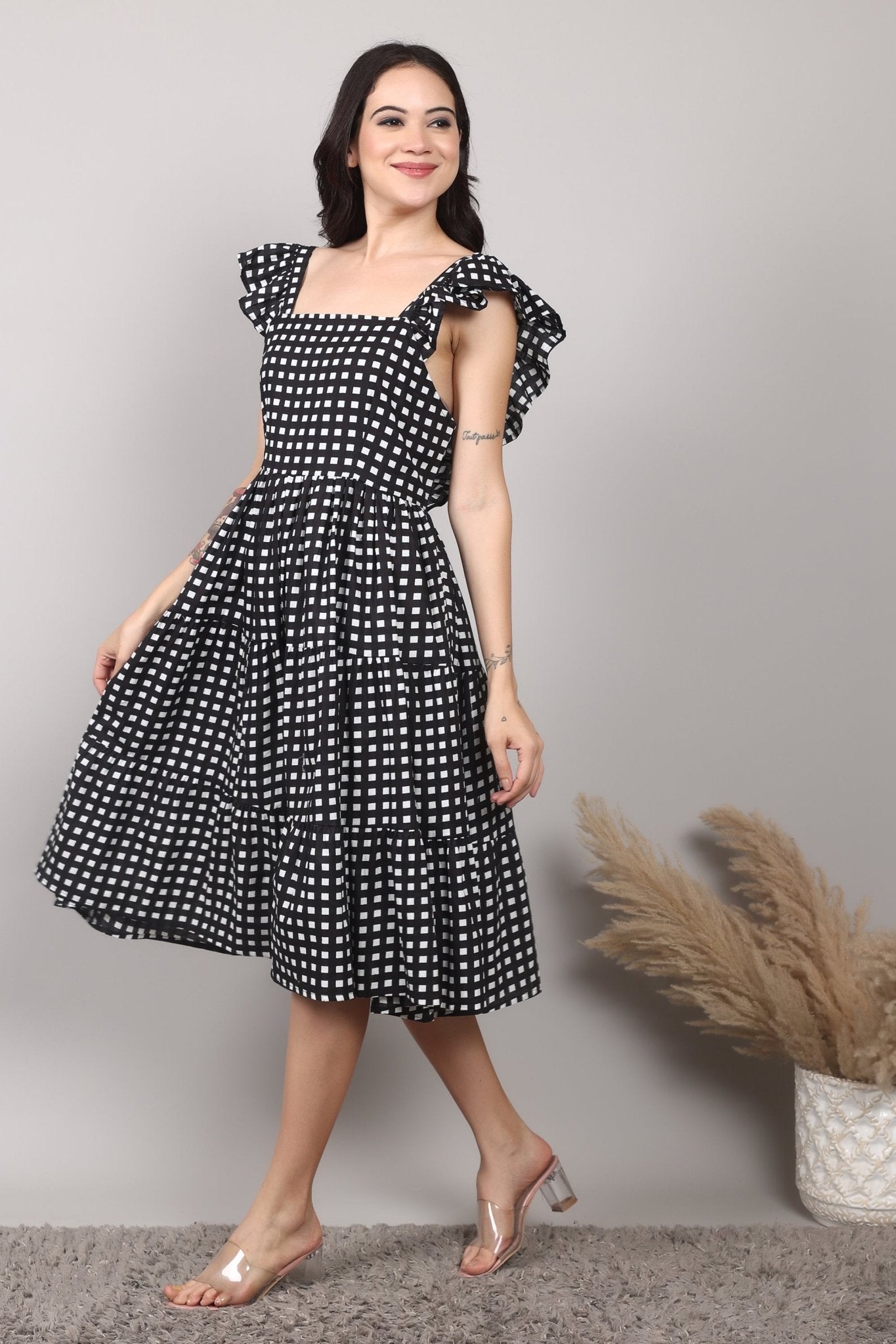 Black-and-white gingham cotton midi dress with square neckline, ruffled cap sleeves, fit-and-flare silhouette, tiered skirt, and a fixed bow at the back.